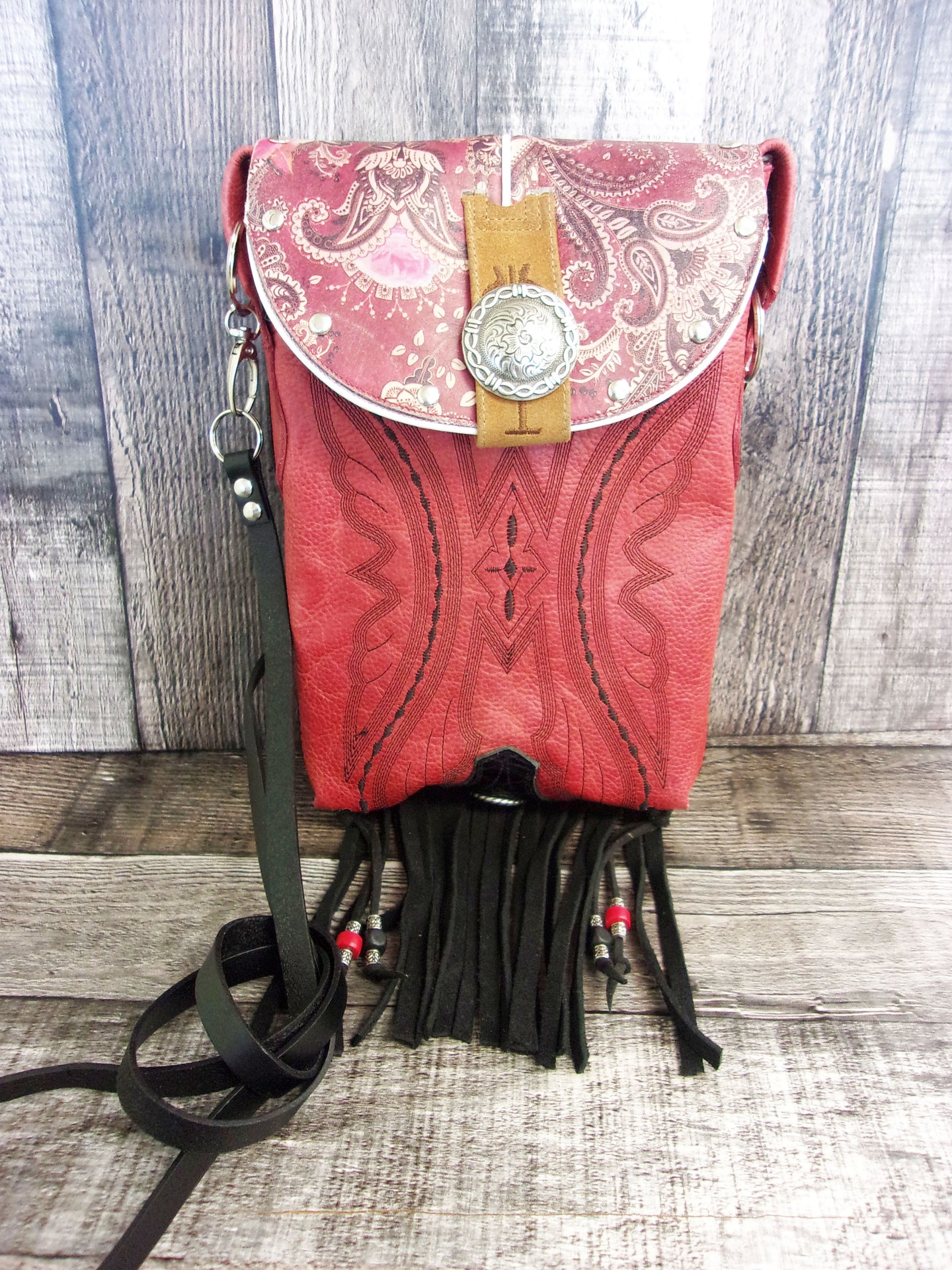 A red crossbody hipster bag made from recycled cowboy boots with fringe detailing and a leather strap.